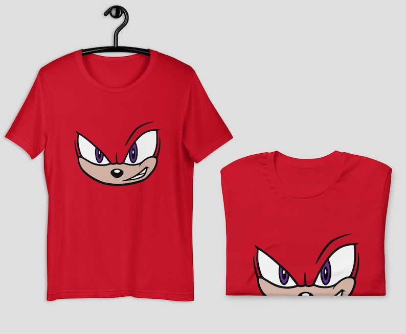 May include: Red t-shirt featuring a cartoon face with white eyes, purple pupils, and a tan muzzle. The design is a close-up of a character's face. The shirt is displayed on a black hanger and folded.