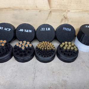 May include: Black ammunition storage containers labelled with white text for .45 ACP, .40 S&W, .22 LR, and 9MM. The containers are filled with various types of ammunition. A two-tone container is also present, labelled .22 LR.