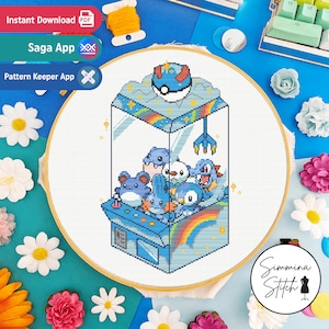 Pode incluir: Padrão de ponto cruz com uma máquina de garra azul cheia de personagens de desenhos animados azuis, um arco-íris e uma Poké Bola no topo. O design está dentro de um bastidor de bordado, rodeado por flores e texto que diz "Download Instantâneo", "Saga App" e "Pattern Keeper App".
