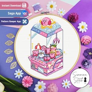 Op de afbeelding: Een kruissteekpatroon met een roze en blauwe klauwmachine gevuld met roze Kirby-karakters. De klauwmachine is omringd door wolken en sterren. Het patroon is ingelijst in een houten hoepel.