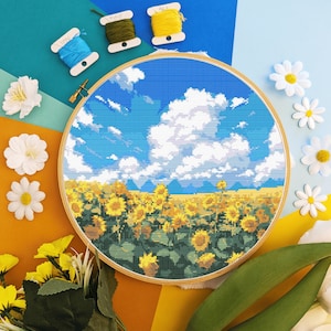 Może przedstawiać: Obręcz do haftu krzyżykowego z kolorowym obrazem pola słoneczników pod błękitnym niebem z białymi chmurami. Haft jest oprawiony w drewniany obręcz.