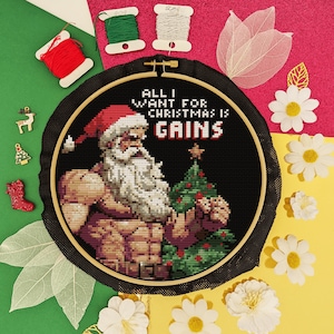 May include: A black and white cross-stitch embroidery hoop with a muscular Santa Claus holding a Christmas tree. The text reads "All I Want For Christmas Is Gains".