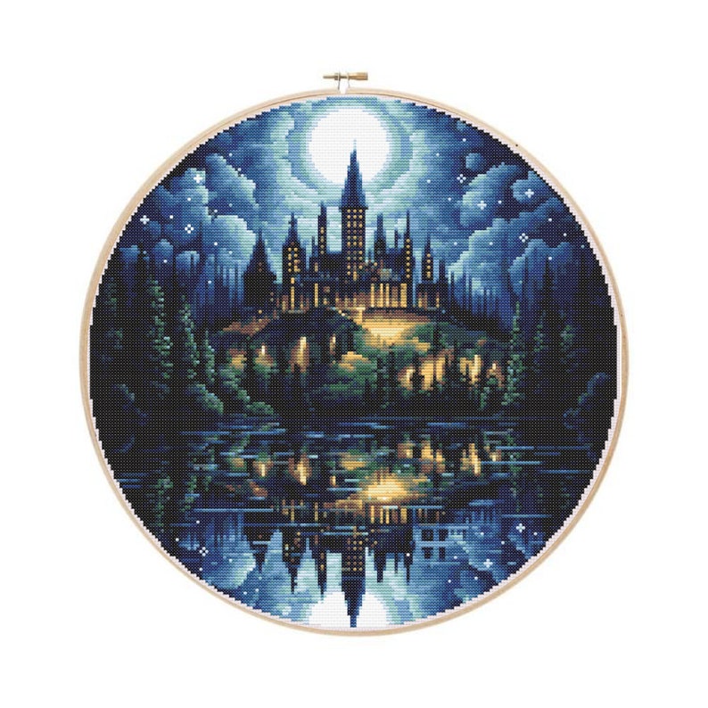 May include: A cross-stitch embroidery of a castle scene at night, set in a wooden hoop. The castle is illuminated with warm lights, reflected in the water below. The sky is dark blue with a full moon and stars.