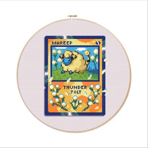 May include: A cross-stitch embroidery of a Mareep Pokémon card. The card features a yellow and blue design with the text "Mareep" and "Thunder Jolt". The embroidery is set in a wooden hoop.