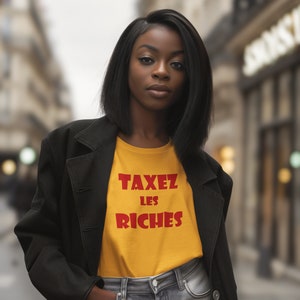 May include: A woman wearing a black jacket over a yellow t-shirt with the text "TAXEZ LES RICHES" in red. She is standing in a city street.