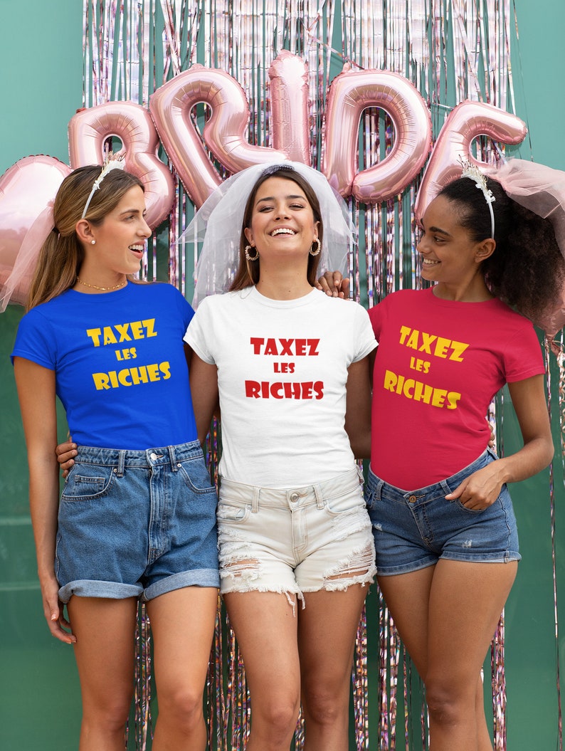 May include: Three friends wearing matching t-shirts with the text "Taxez Les Riches" in yellow and red letters. The shirts are blue, white, and red. The friends are smiling and posing for a photo.