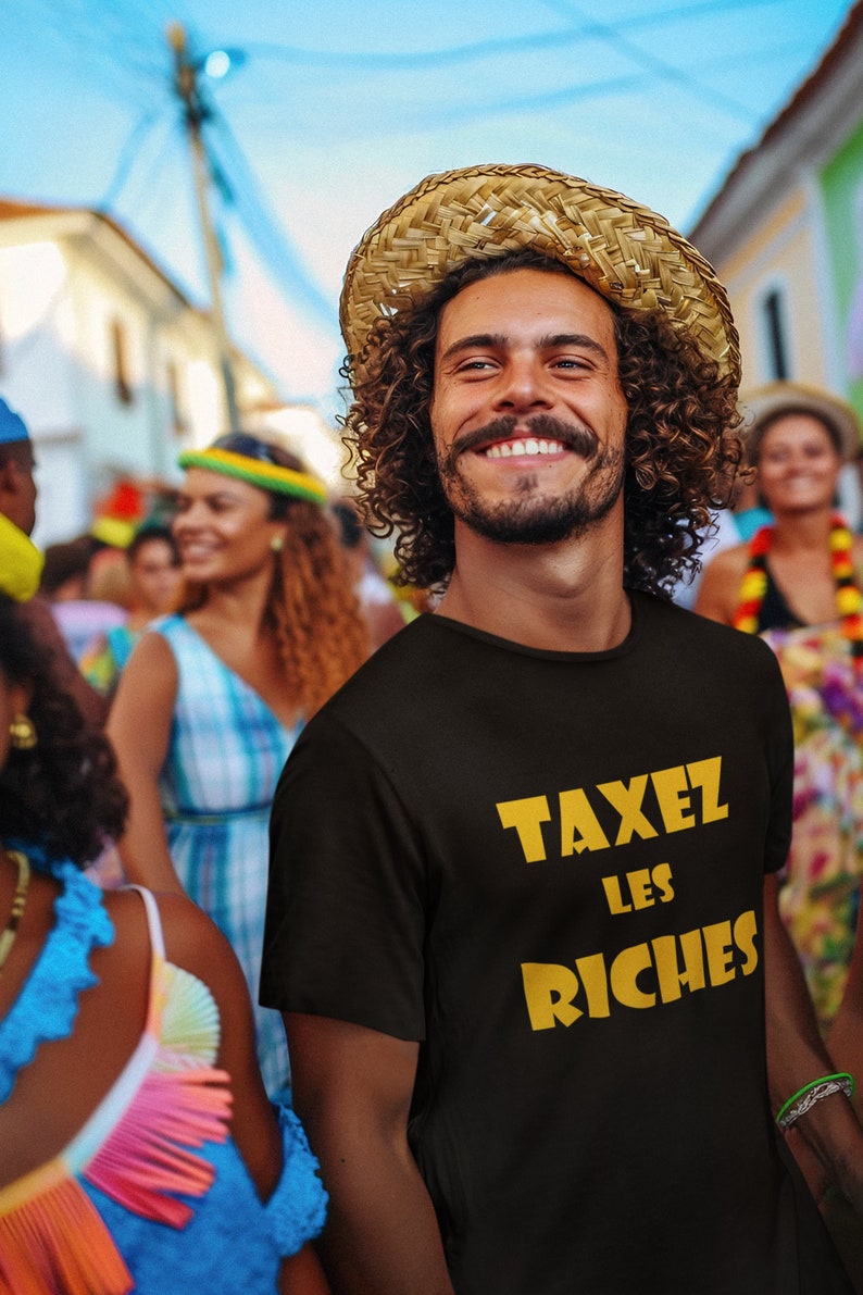 May include: A person wearing a black t-shirt with the text "TAXEZ LES RICHES" in yellow letters. The person is smiling and wearing a straw hat.