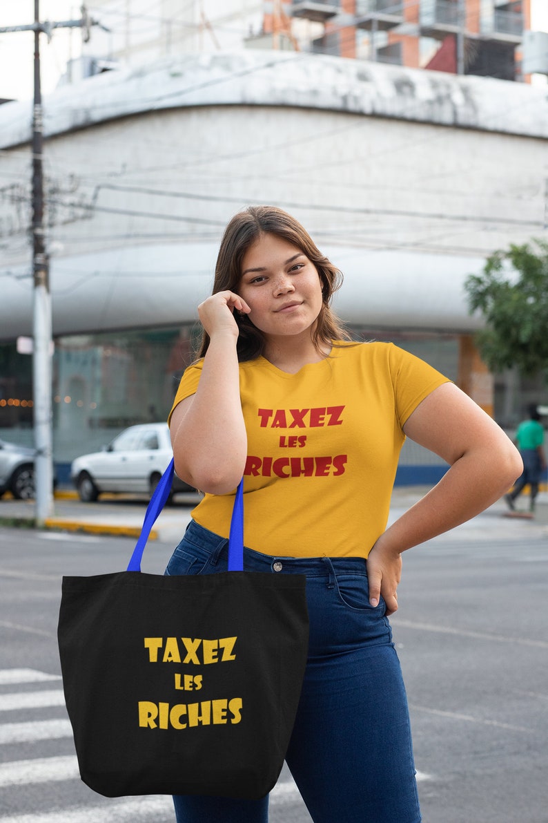 May include: A person wearing a yellow t-shirt with the text "TAXEZ LES RICHES" in red. They are holding a black tote bag with the same text in yellow.