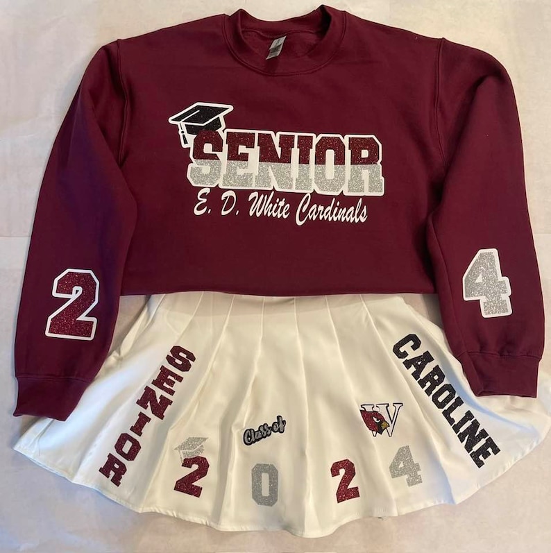 May include: Burgundy sweatshirt with "SENIOR" and "E.D. White Cardinals" in silver glitter lettering. The sweatshirt has a white pleated skirt with "SENIOR", "Class of 2024", and "CAROLINE" in silver glitter lettering.