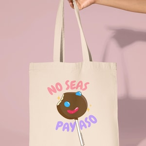 Pode incluir: Uma bolsa tote bege com um gr&aacute;fico de pirulito marrom e branco e o texto "No seas payaso" em letras rosa e roxo.