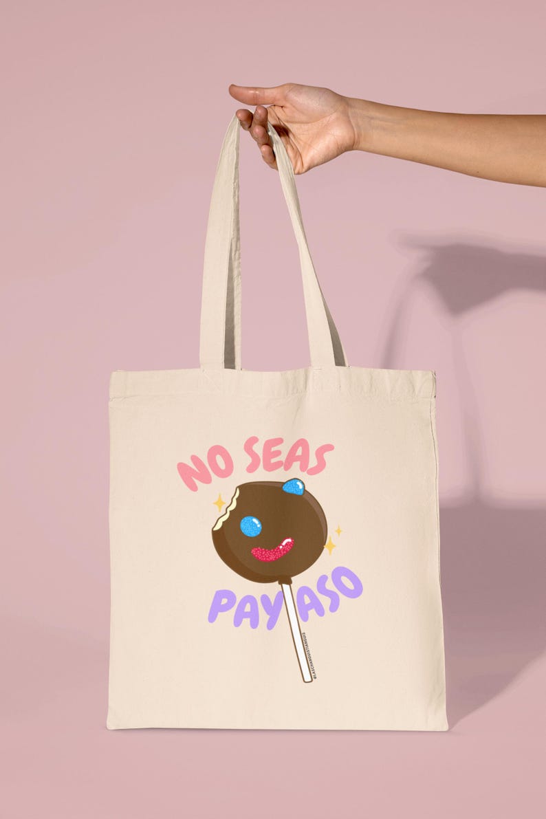 Pode incluir: Uma bolsa tote bege com um gr&aacute;fico de pirulito marrom e branco e o texto "No seas payaso" em letras rosa e roxo.