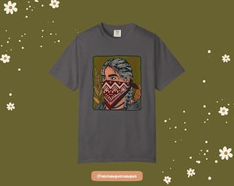 May include: Dark gray t-shirt featuring a graphic of a person wearing a red bandana with a detailed design. The person has braided hair and is framed by wheat and corn. The shirt has a crew neck.