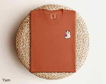 以下が含まれることがあります： さび色のTシャツに、コーヒーカップを持った小さな白い幽霊が描かれています。幽霊は小さな角が2本あります。Tシャツには「Coffee Clouds」という文字がタグに印刷されています。