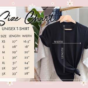 Może przedstawiać: Tabela rozmiar&oacute;w dla koszulki unisex. Tabela pokazuje długość i szerokość w calach dla rozmiar&oacute;w XS, S, M, L, XL, 2X i 3X. Na wieszaku widoczna jest czarna koszulka.