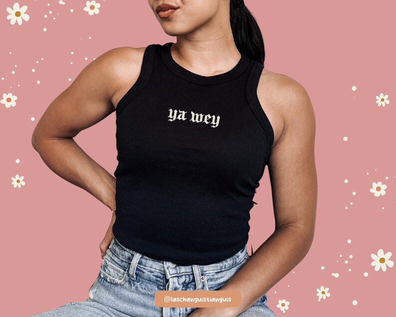 K&ouml;nnte beinhalten: Schwarzes geripptes Tanktop mit dem Text "ya wey" in gotischer Schrift. Das Oberteil ist &auml;rmellos und hat einen runden Ausschnitt. Das Model tr&auml;gt eine blaue Jeans. Der Hintergrund ist rosa mit wei&szlig;en Blumengrafiken.