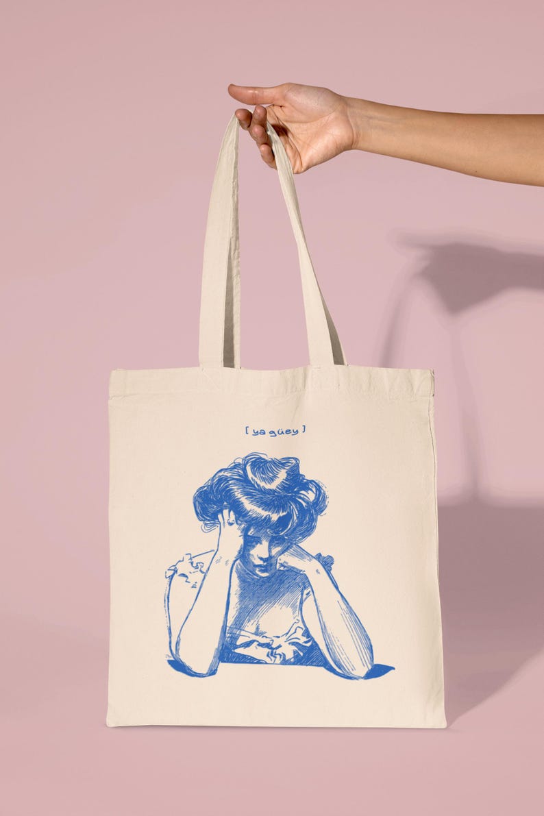 May include: A white canvas tote bag with blue text that reads "[ya quey]" and a blue illustration of a woman with her head in her hands.