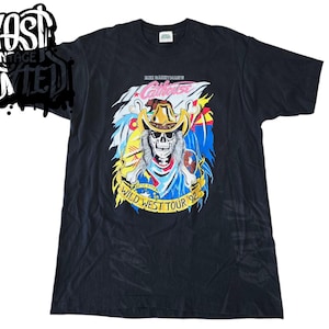 Peut inclure: T-shirt noir avec un motif coloré d'un crâne portant un chapeau de cowboy et le texte "Alice Cooper's Wild West Tour '92".