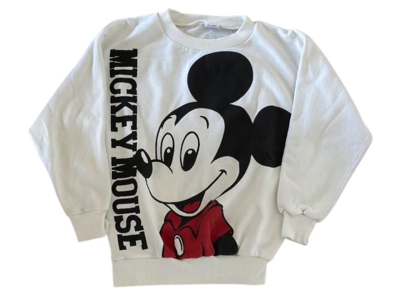 May include: White sweatshirt featuring a large graphic of Mickey Mouse in black, red, and white. The words "MICKEY MOUSE" are printed vertically on the left sleeve. The sweatshirt has a crew neck and long sleeves.