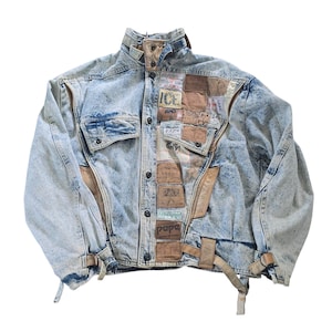 May include: Acid wash denim jacket with patches and leather accents. The jacket features a button-up front, two chest pockets, and adjustable waist straps. Patches include the words "ICE", "Reebok", and "papa".