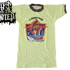 Könnte beinhalten: Vintage gelbes T-Shirt mit braunem Besatz und dem Aufdruck "I Survived the Shock Wave Six Flags". Die Grafik zeigt eine Achterbahn in Rot, Blau und Weiß.