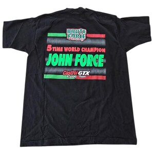May include: Black t-shirt featuring the text "BRUTE FORCE Racing" and "5 TIME WORLD CHAMPION JOHN FORCE". The shirt also displays the "Castrol GTX Racing Team" logo in green and red. The shirt is a vintage item.