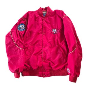 May include: A red satin bomber jacket with a button-up front, featuring a team logo patch on the chest and left sleeve. The jacket has a ribbed collar, cuffs, and hem. The jacket is a size large.