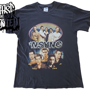May include: Black vintage t-shirt featuring a photo of the boy band *NSYNC. The band members are pictured in a circle with the band's name in large, silver letters. The names of each band member are listed below the photo: Joey, Lance, Justin, Chris, and JC.