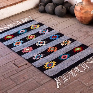 May include: A black and gray rug with colorful diamond patterns. The rug has white fringe on the edges.
