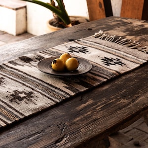 May include: A rustic wooden table with a white and brown patterned runner. A small plate with three yellow fruit sits on the runner.