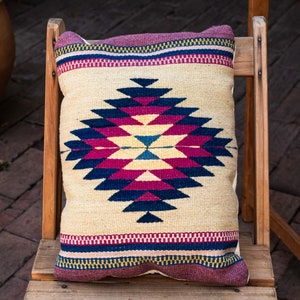 May include: A beige throw pillow with a geometric pattern in shades of pink, blue, and black. The pillow is sitting on a wooden chair.