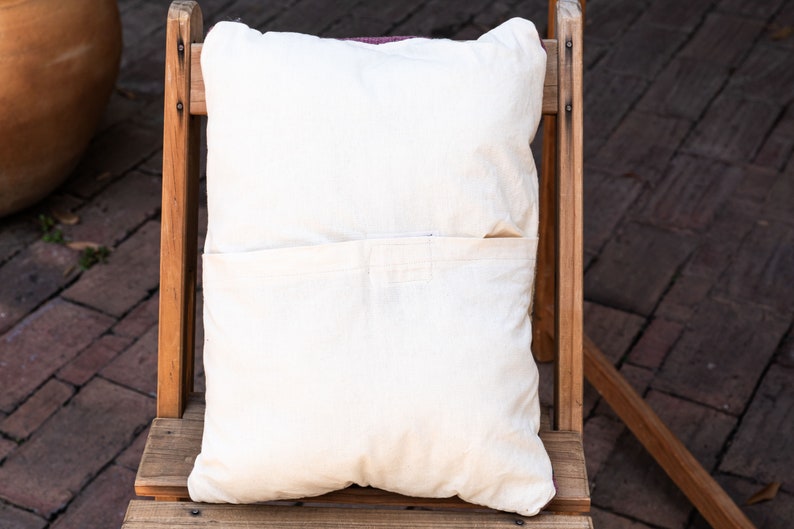 May include: A white pillow with a pocket on the back, sitting on a wooden chair. The chair is made of natural wood and has a rustic look.