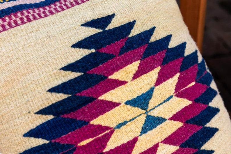 May include: Close-up of a woven pillow with a geometric pattern in shades of blue, pink, and cream.