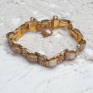 May include: A gold-tone bracelet with a chain closure and white rectangular accents. The bracelet is made of metal and has a delicate design.