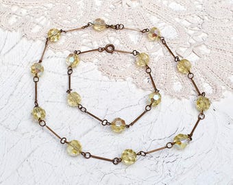 May include: A delicate gold necklace with a chain made of small, straight bars and a series of faceted, pale yellow glass beads.