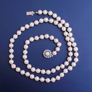 May include: A white pearl necklace with a silver clasp and a small silver flower charm. The necklace is on a blue background.