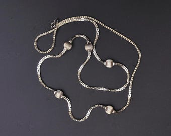 May include: A silver-toned necklace with a delicate chain design. The necklace features five textured, spherical beads evenly spaced along the chain. The jewelry is displayed against a dark background, highlighting its metallic sheen.