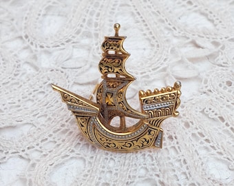 May include: A gold and silver ship brooch with intricate details. The ship has a tall mast and sails, and the bow is decorated with a floral design.