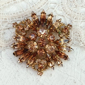May include: A large, gold-toned brooch with a cluster of brown and clear rhinestones in a starburst design.