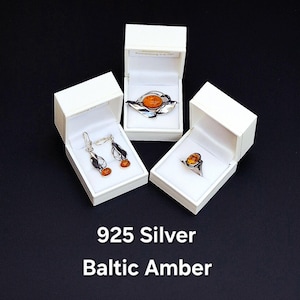 May include: Jewelry set featuring 925 silver and Baltic amber. The set includes a ring, earrings, and a brooch, each displayed in a white box. The amber stones have a warm, orange hue. The text "925 Silver Baltic Amber" is at the bottom.