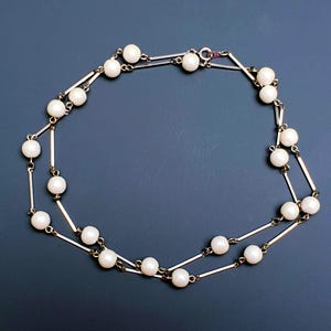 May include: A delicate gold chain necklace with white pearls. The chain is made of two strands with small bars connecting the pearls.