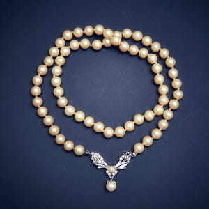 May include: A pearl necklace with a silver pendant featuring a delicate design. The necklace is made of white pearls and has a classic look.