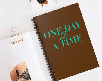May include: A brown spiral notebook with the text "ONE DAY at a TIME" in turquoise blue lettering.