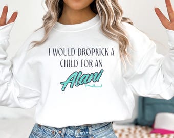 May include: White sweatshirt with the text "I WOULD DROPKICK A CHILD FOR AN Alani NU" in black and teal. The sweatshirt is long-sleeved and has a crew neck. The text is centered on the front of the shirt.