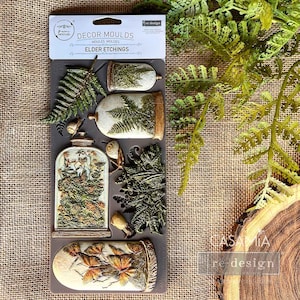 May include: A silicone mold for crafting, featuring a set of botanical designs. The mold includes a fern, a jar with a fern inside, a jar with butterflies, and a jar with a fern and a butterfly. The mold is labeled "Decor Moulds, Elder Etchings".