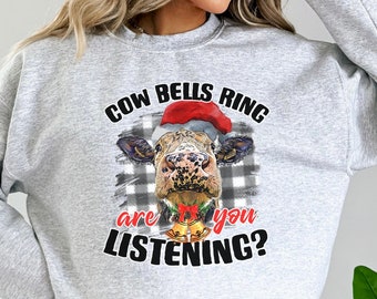 May include: Gray sweatshirt with a black and white checkered background and a cow wearing a Santa hat. The text on the sweatshirt reads "Cow Bells Ring Are You Listening?"