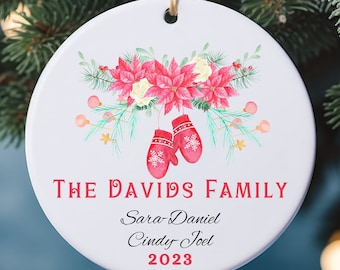 May include: White ceramic Christmas ornament with a red poinsettia and holly design. The ornament reads "The Davids Family" with the names "Sara, Daniel, Cindy, Joel" and the year "2023".