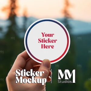May include: A hand holds up a white round sticker with a blue and red border. The sticker has the text "Your Sticker Here" in red letters. The background is blurred and shows a forest and mountains.