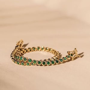 Op de afbeelding: Een gouden kettingarmband met smaragdgroene edelstenen. De armband is gemaakt van een delicate ketting met kleine, ronde edelstenen.