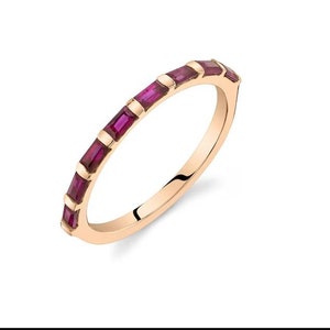 Puede incluir: Un anillo de banda de oro con una fila de pequeñas piedras de rubí rectangulares engastadas alrededor de la banda.