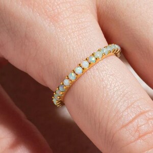 Könnte beinhalten: Ein Goldring mit einer Reihe weißer Opal-Steine.